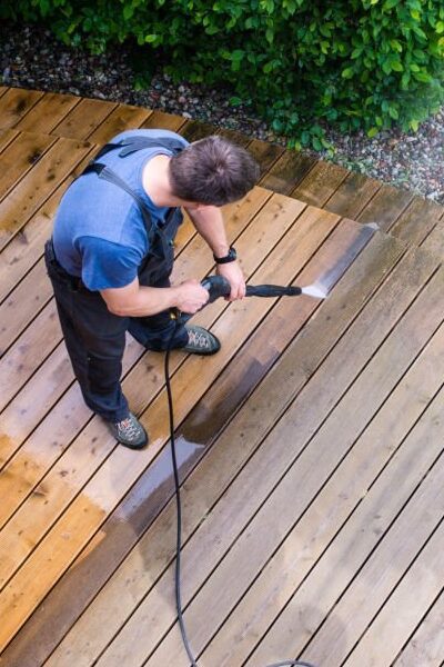 man cleaning terrace with a power washer - high water pressure cleaner on wooden terrace surface